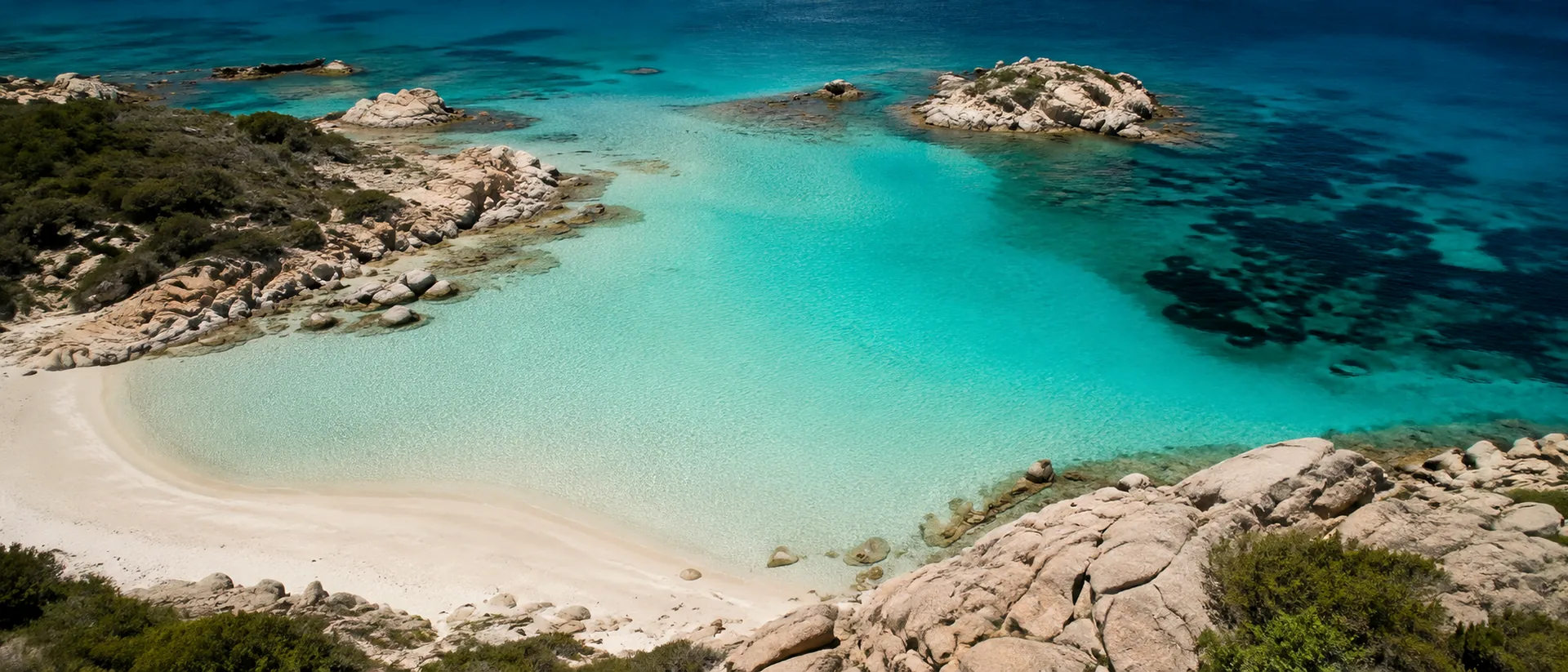Aerial view of a turquoise Costa Smeralda bay with pale sand and granite rocks.