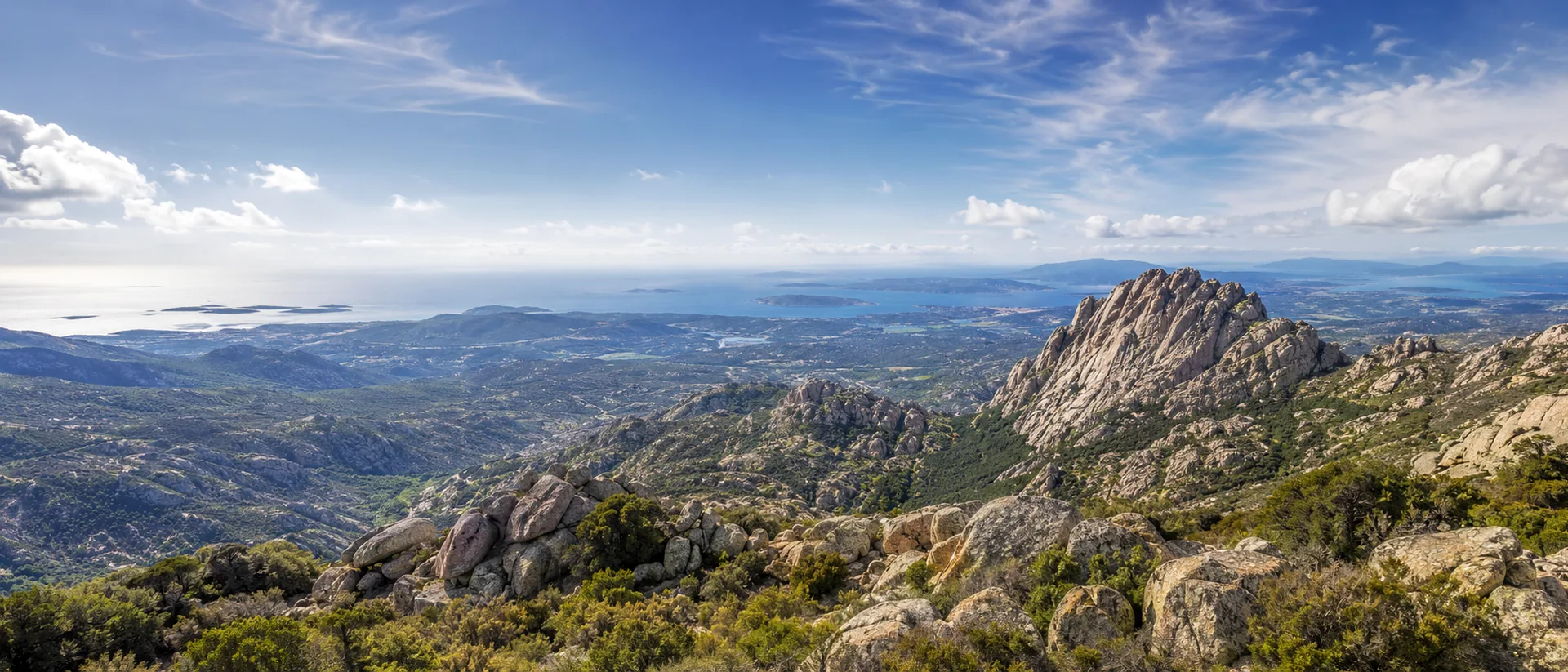 Wide mountain panorama over northern Sardinia, granite peaks and distant sea.