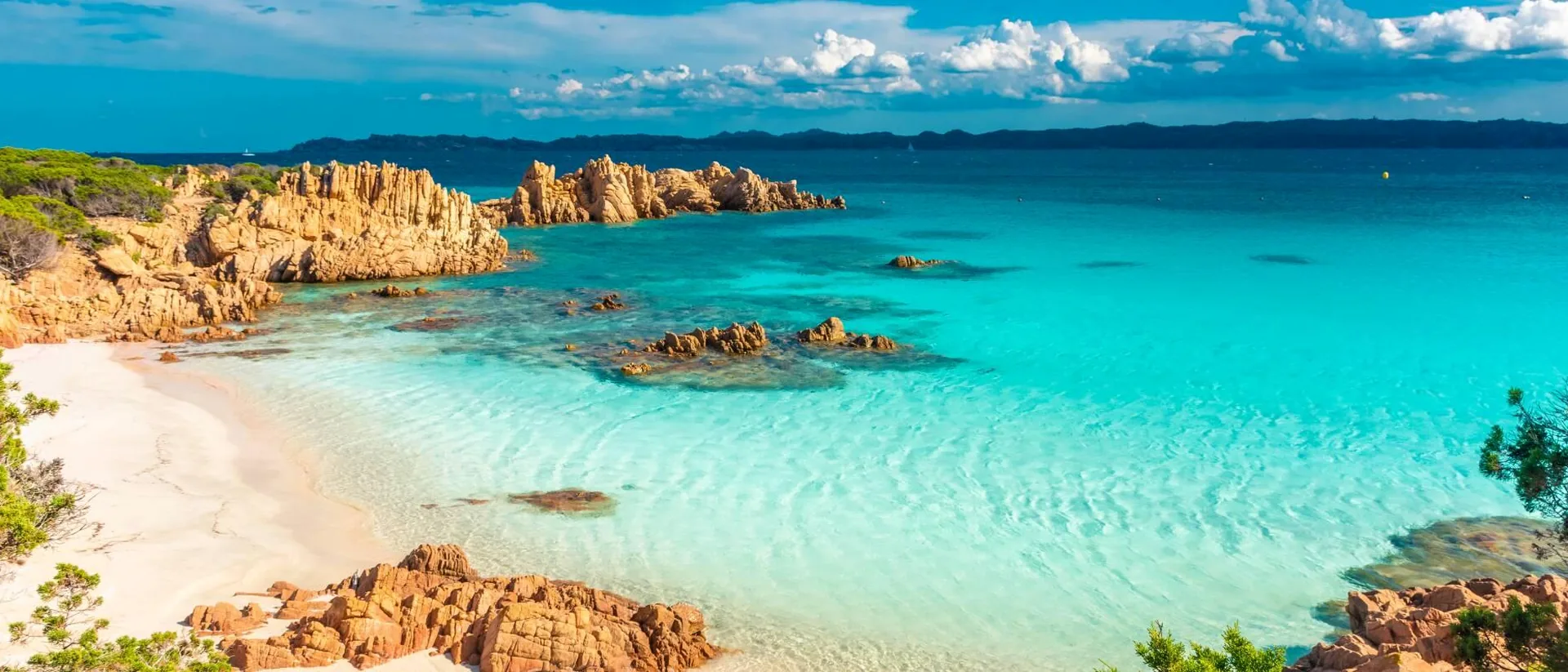 Costa Smeralda beach with vivid turquoise water, pale sand and golden rocks.