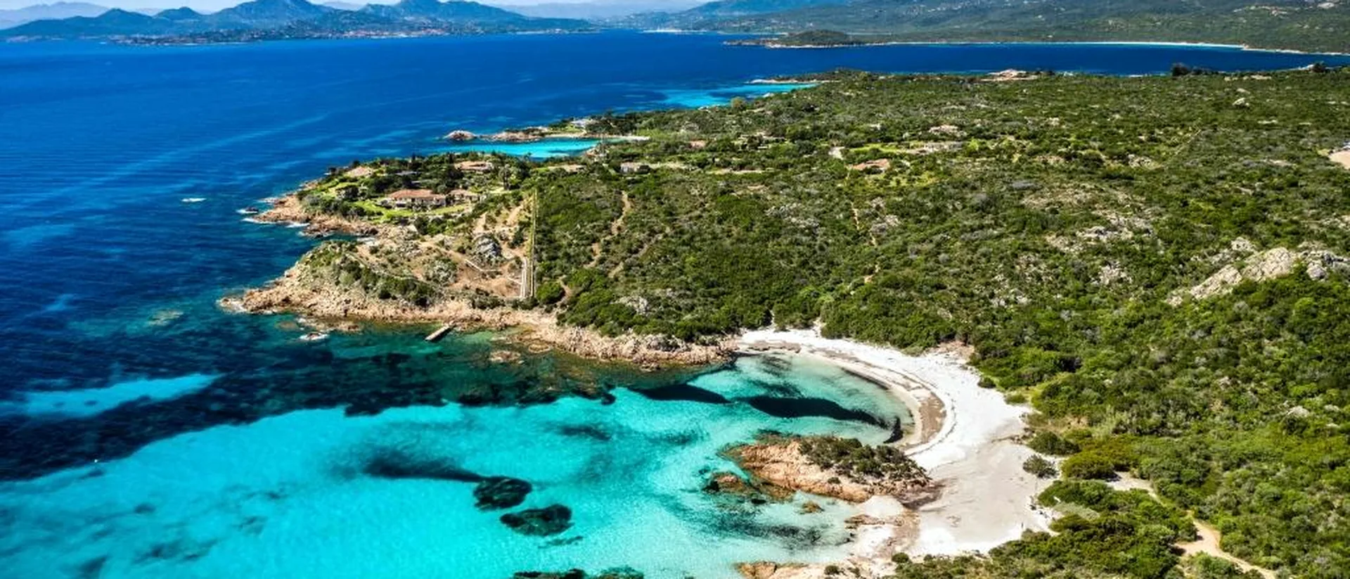 Aerial view of a wild Sardinian cove with turquoise water, beach and green coastline.