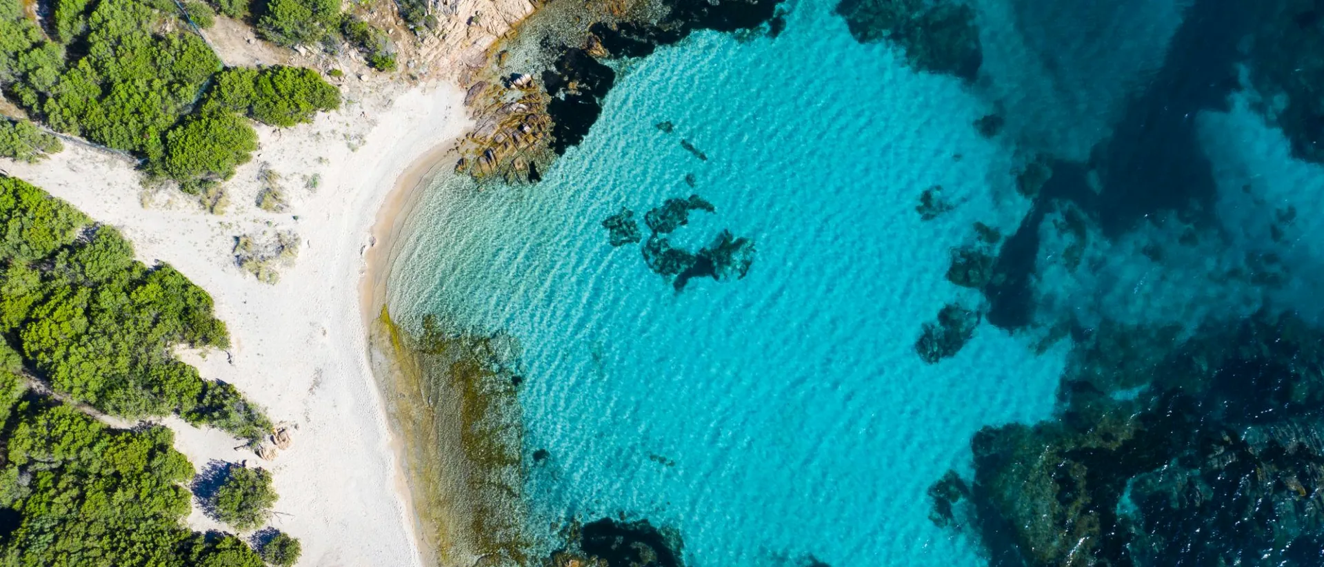 Top-down view of a sandy cove and transparent blue-green water in Sardinia.