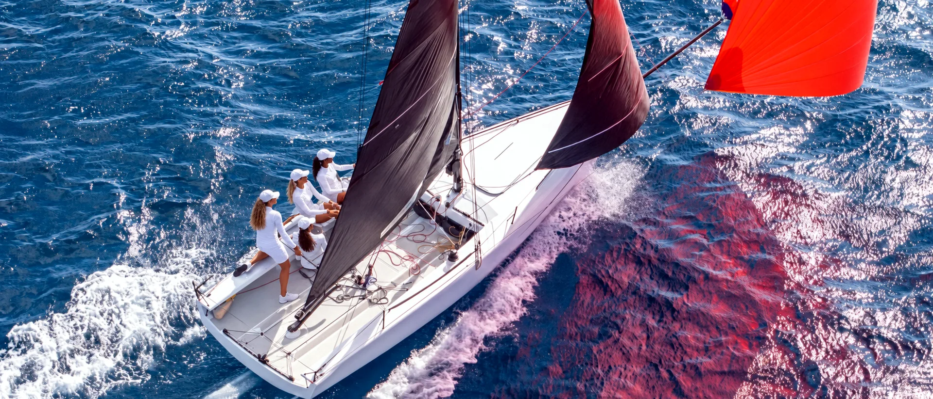 White sailing boat under black sails and an orange spinnaker on sparkling blue water.