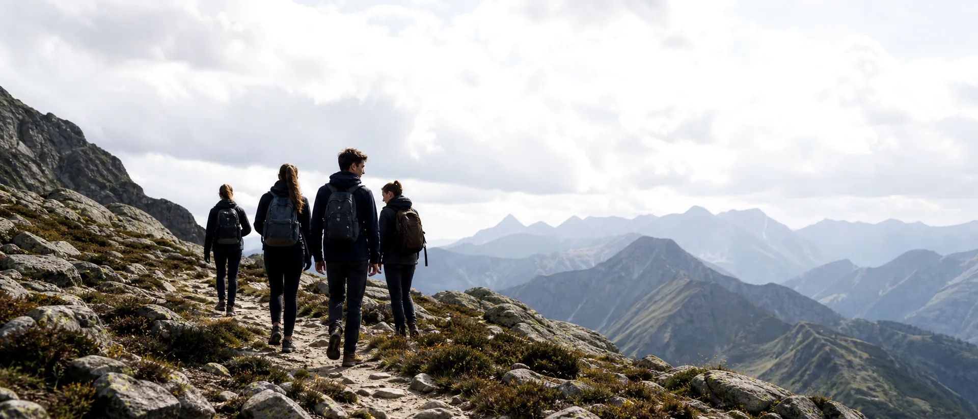 Hikers walking along a high mountain trail under a bright sky.
