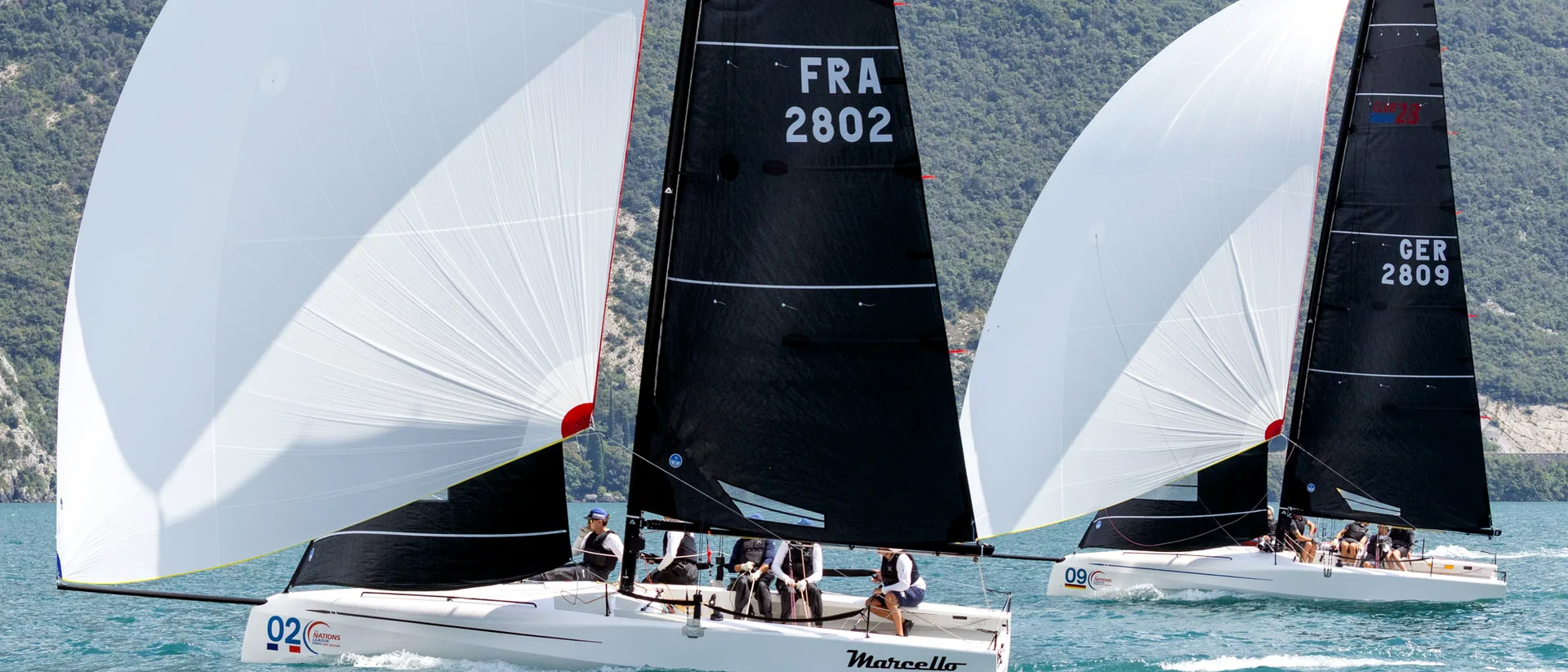 Club racing sailboats with black sails and white spinnakers crossing the water.